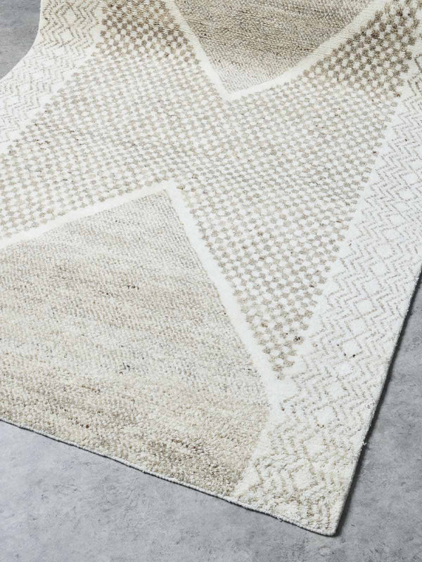 A stunning hand-knotted wool rug by Tribe Home. A geometric pattern in ivory and taupe runs across the middle and sides, highlighting the artistry of the weaving.
