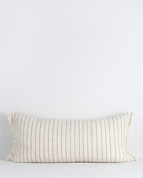 A lengthy cotton lumbar cushion, with regular vertical blue stripes across a cream background. The cushion is fringed at the edges, which adds softness and sophistication. By Baya