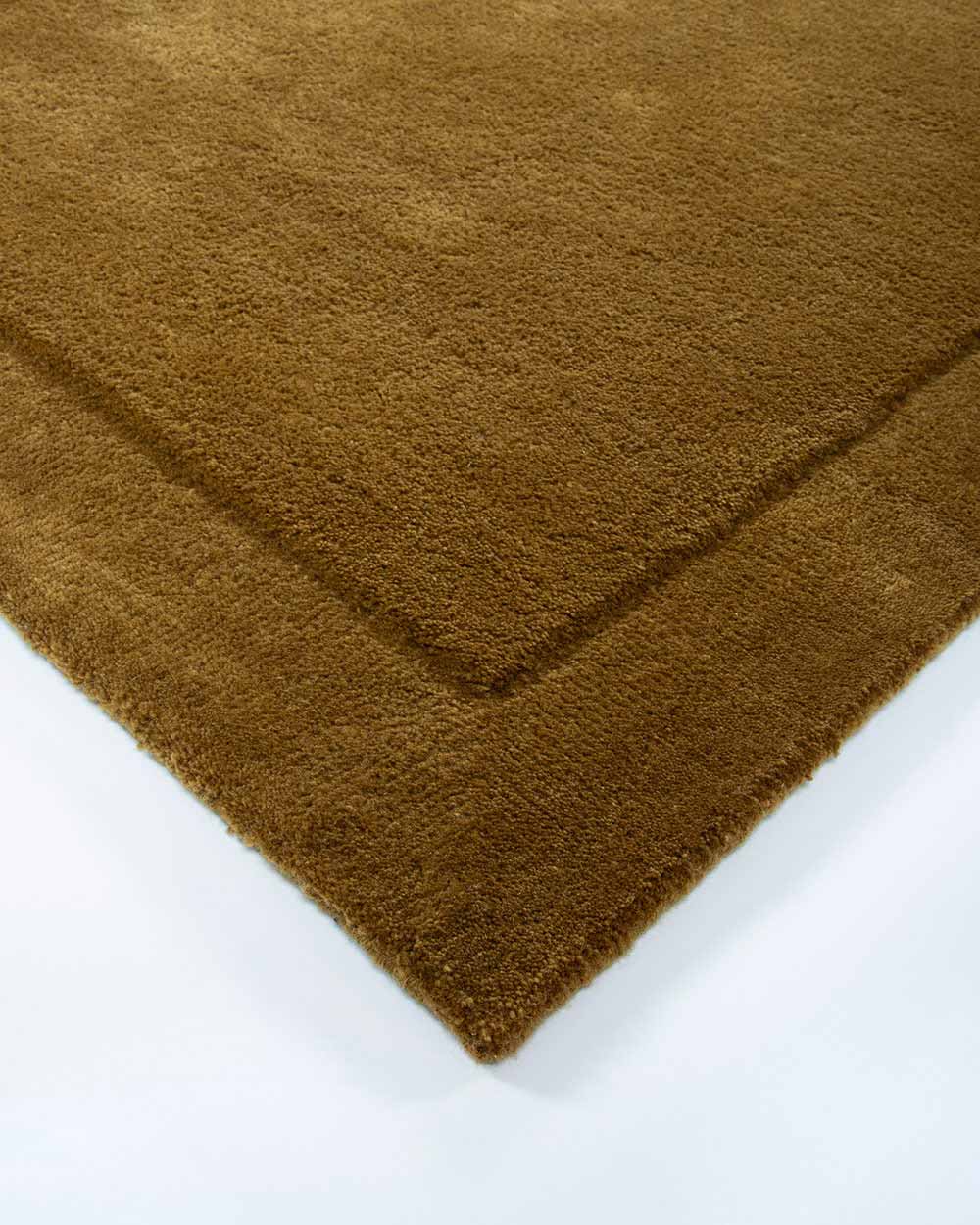 The corner of the Norfolk rug, 100% wool in Brass by Baya. The minimalist cut-pile border adds depth to this stunning piece