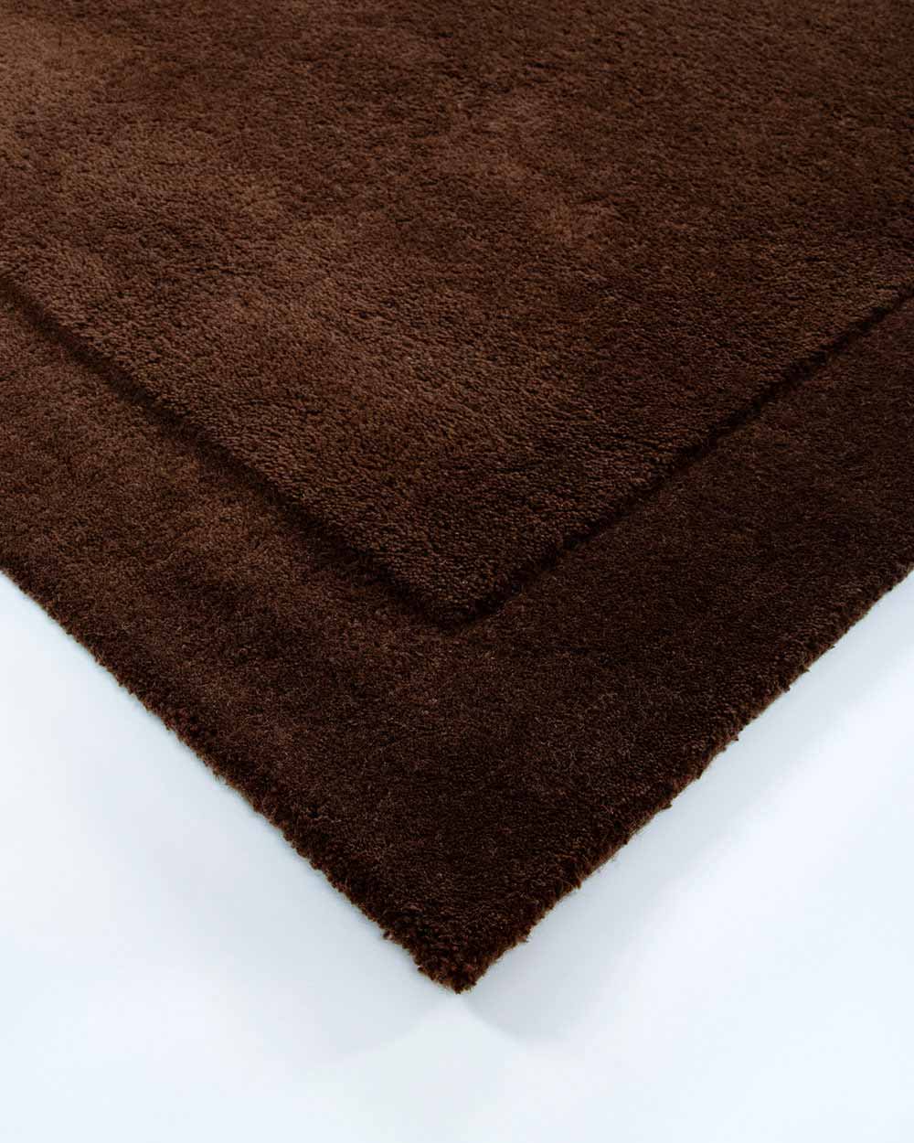 The corner of the Norfolk floor rug in the shade Chocolate. The border of the rug is cut-pile in a minimalist and refined design.