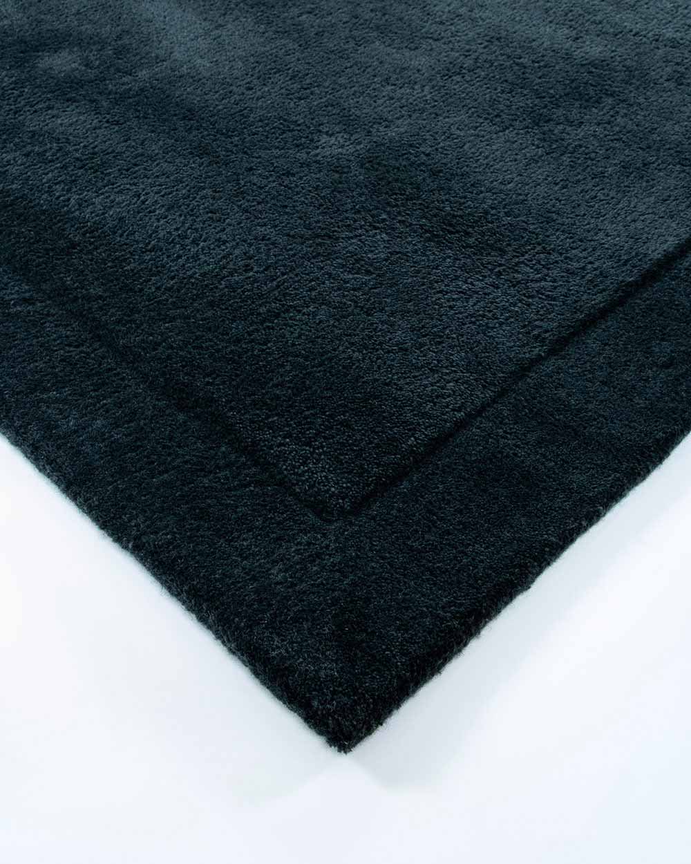 The corner of the Norfolk floor rug by Baya in the shade Ink, a beautiful deep navy blue. The rug is textured and has a flattened edge, bringing interest to the piece