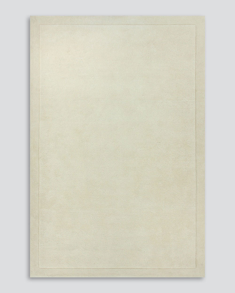 A full image of the Norfolk floor rug in the shade Ivory. The border of the rug is cut-pile in a minimalist and refined design, and the pile of the rug's centre is luxuriously deep.