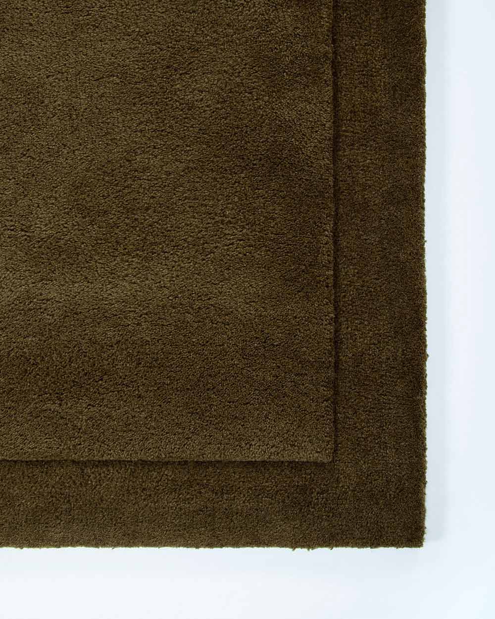 The corner of the Norfolk floor rug in the shade Olive. The border of the rug is cut-pile in a minimalist and refined design.