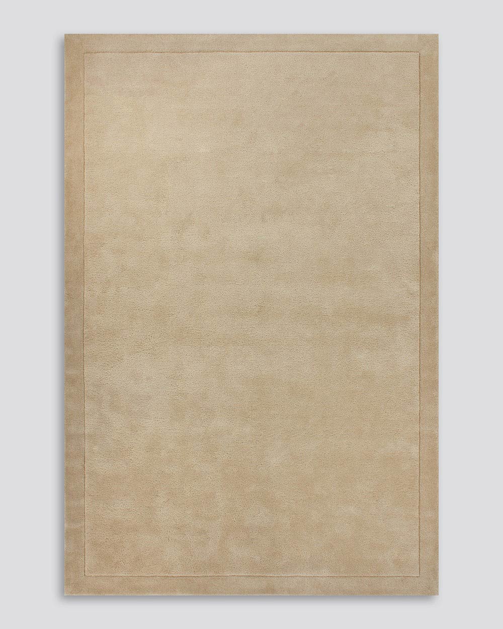 A full image of the Norfolk floor rug in the shade Sand. The border of the rug is cut-pile in a minimalist and refined design, and the pile of the rug's centre is luxuriously deep.