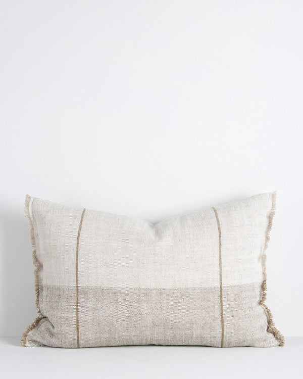 A soft beige and cream linen lumbar cushion with stripes following the edges. There is a soft fringe at the short edges, lending further softness. By Baya