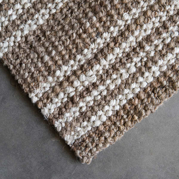 The corner of a hand knotted jute floor rug in natural brown with white washed stripes.