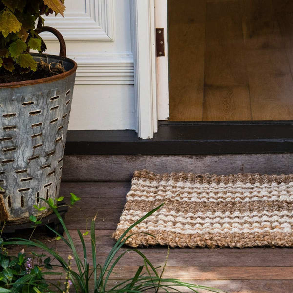 A doorway with an entrance mat in natural brown jute with whitewashed stripes.
