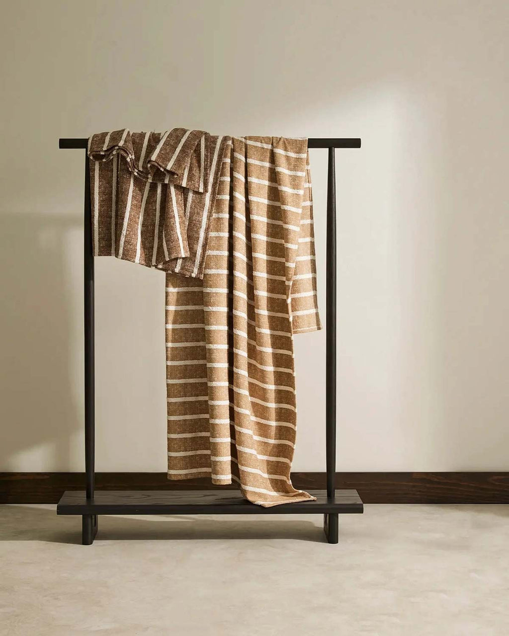 Two Piazza throw blankets, in shades Haze and Earth, by Weave Home, hanging on a clothing rack.
