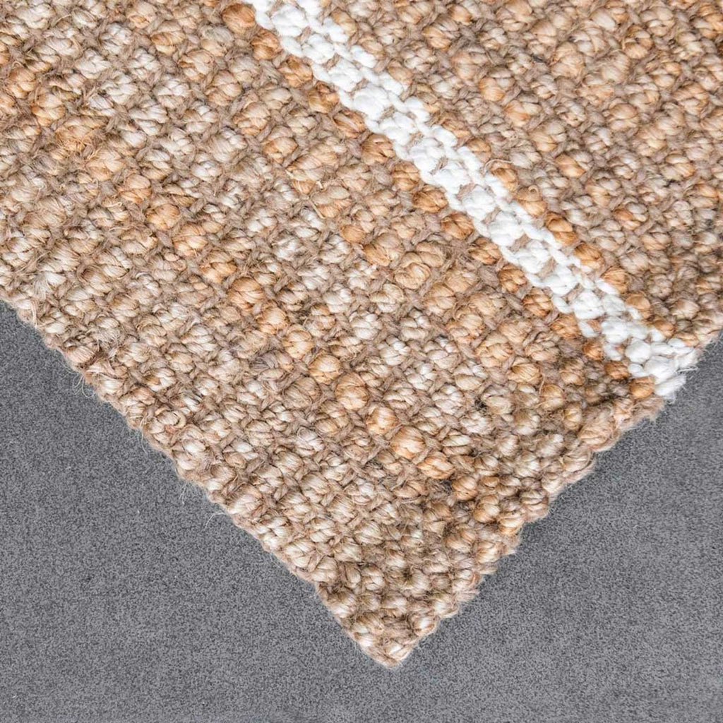 A detailed view of the corner of a hand knotted jute floor rug with a white stripe.