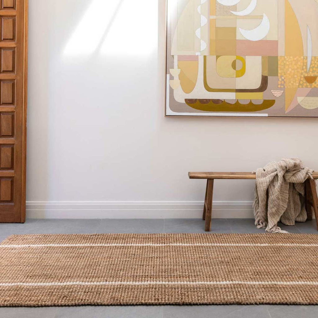A floor runner in a sitting room made of natural jute with minimalist stripes white washed.