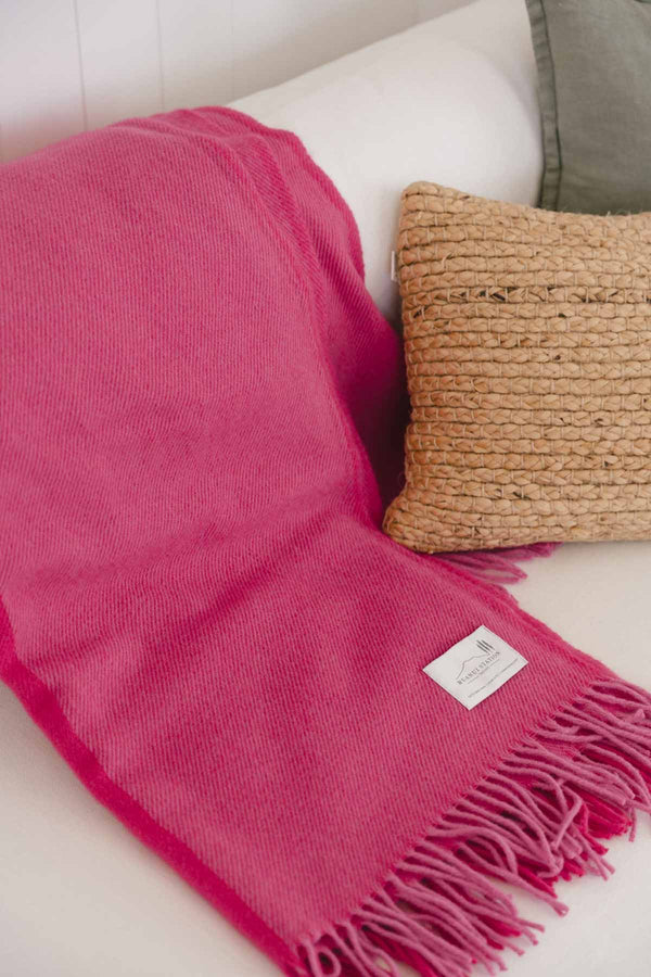 A bright pink lambswool throw blanket from Ruanui Station NZ, folded on a couch.