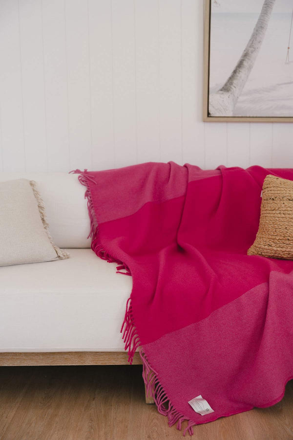 A bright pink throw blanket by Ruanui Station, thrown over the back of a white couch.