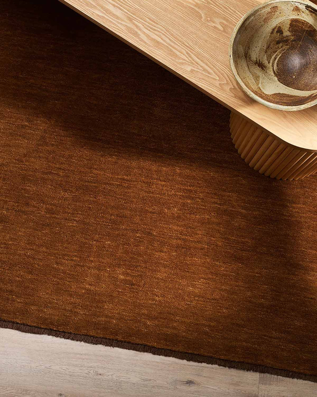 A coffee table on top of a rich red-brown floor rug with a fringed edge.