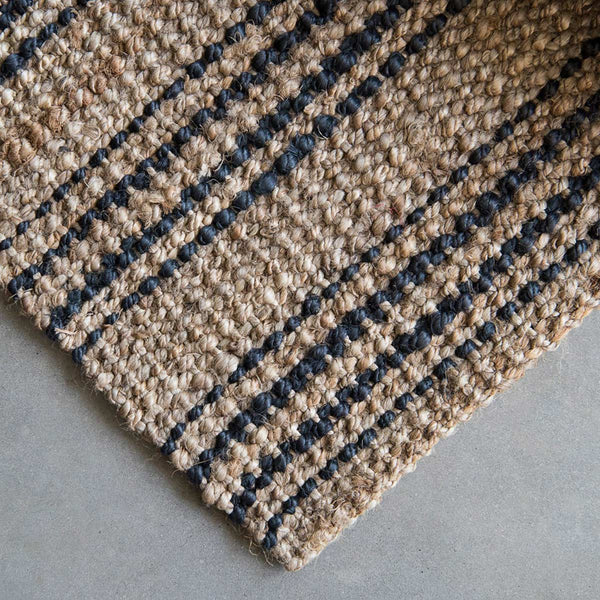 A detailed view of the corner of a natural fibre brown jute floor rug with graphite stripes.