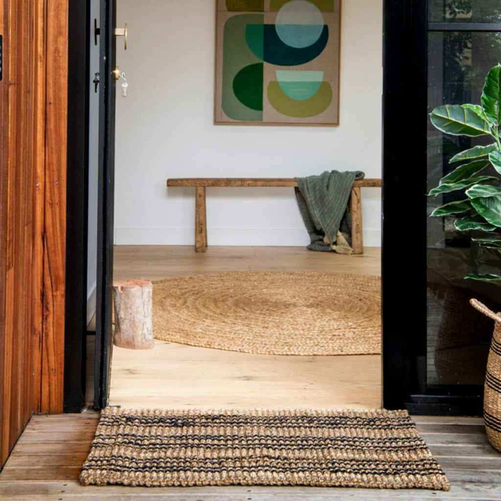 A doorway with an artisanal handmade black and brown striped doormat.