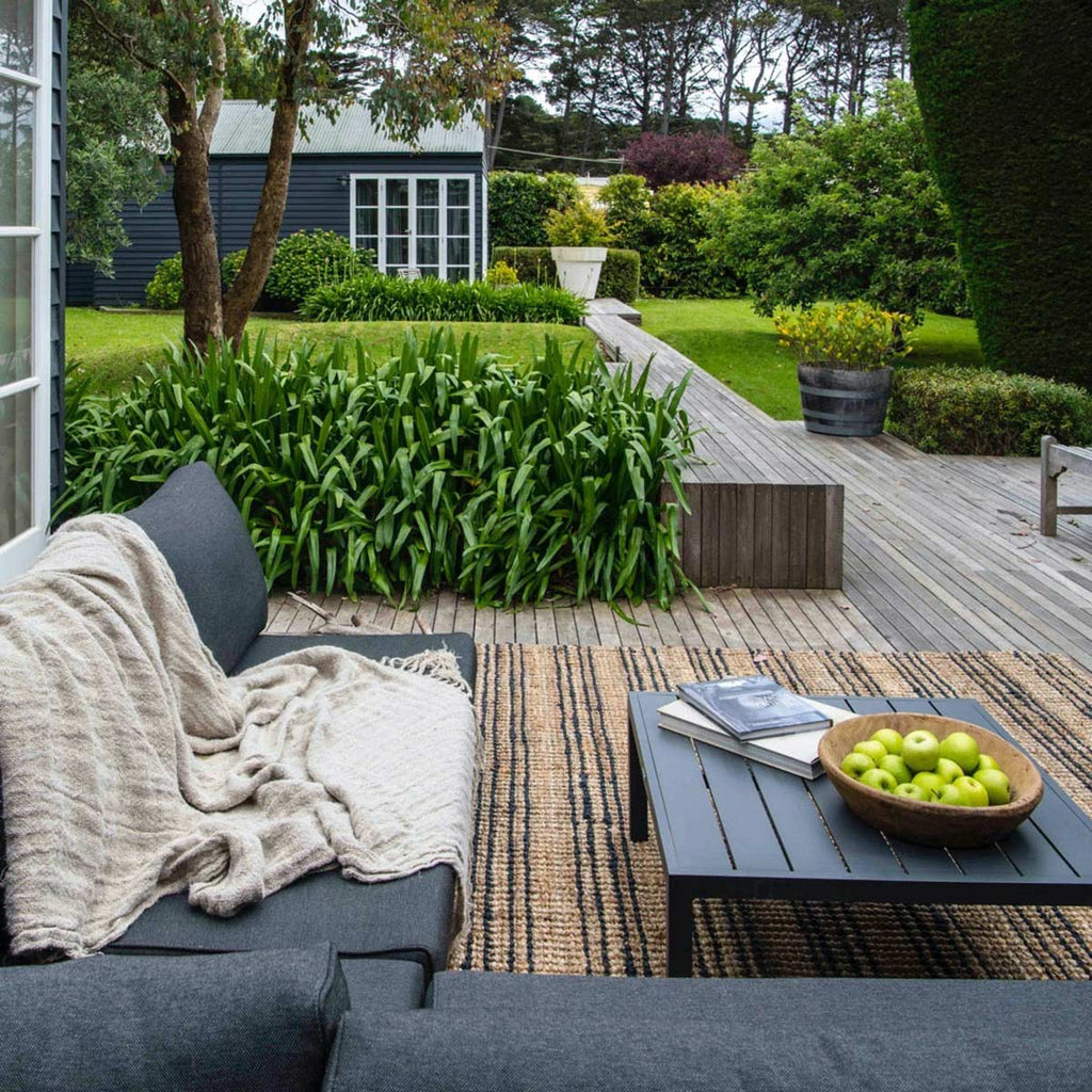 An outdoor deck area with a couch and a jute floor rug with stylish natural brown and black striping.