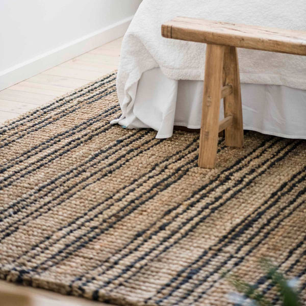 A handknotted black and brown striped jute floor rug in a bedroom.