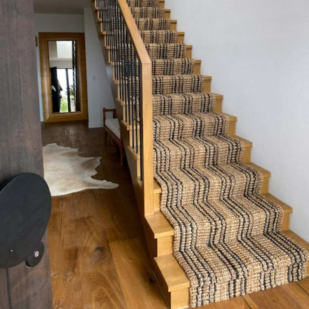 A staircase with a jute runner going down it, with black striping and natural brown jute fibres.
