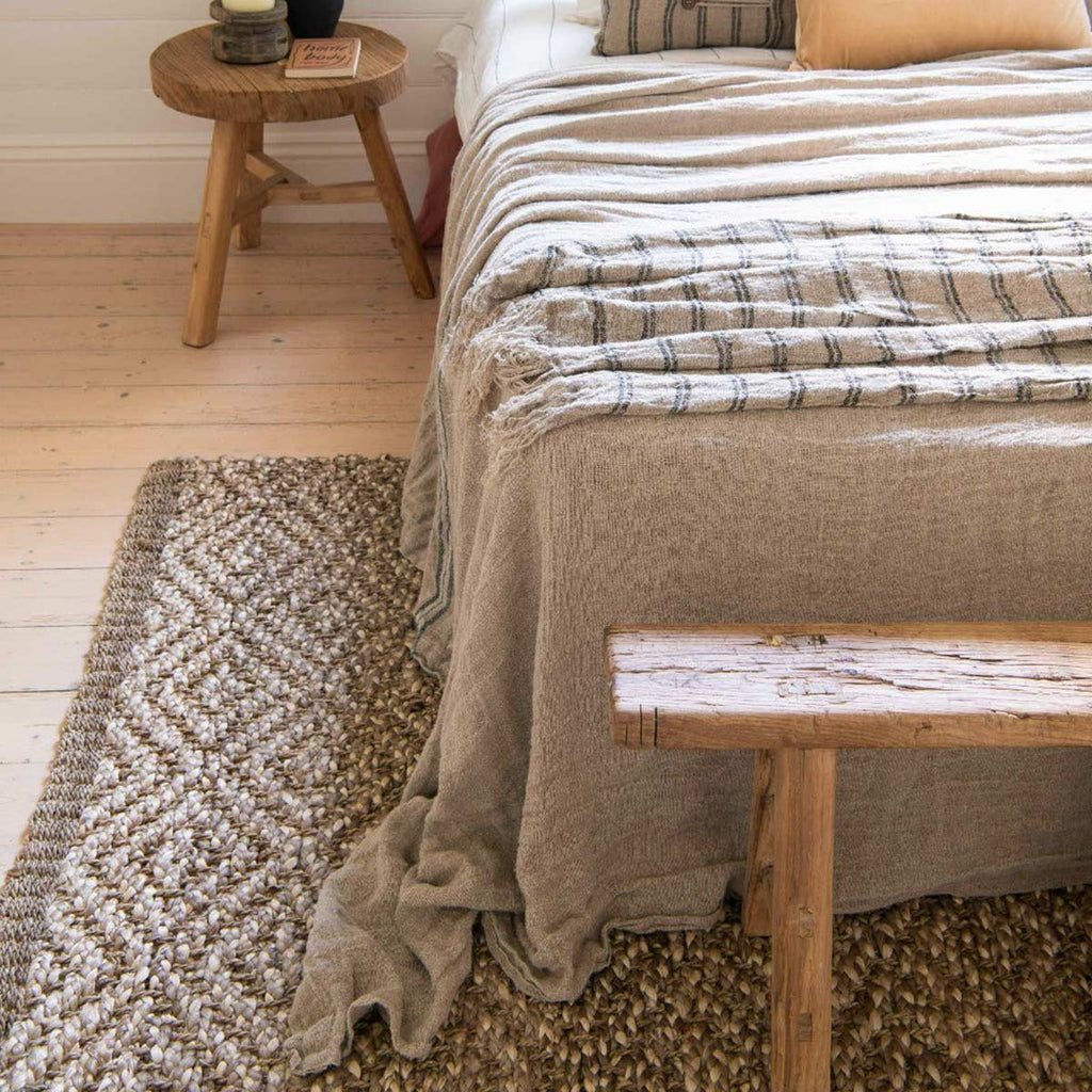 A cosy bedroom with a diamond patterned floor rug in natural jute fibres and a boucle weave.