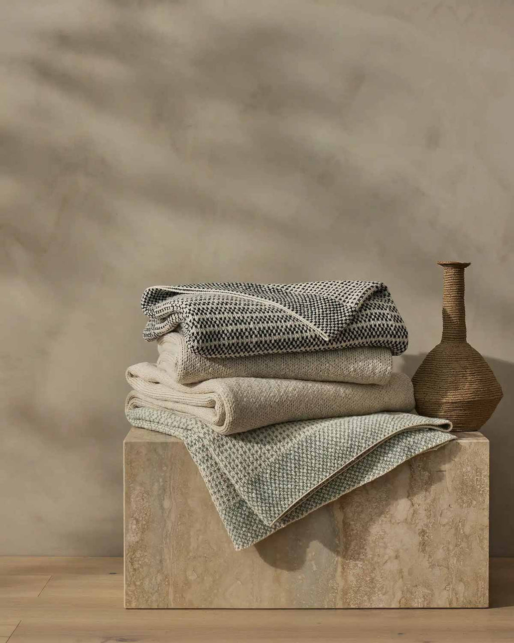 Three cotton knit throw blankets by Weave Home, folded on a stool.