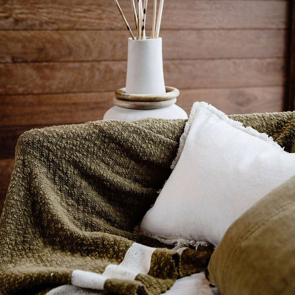 A textured cotton throw blanket in shades of deep warm green and white in a modern living room.