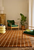 Living room with green armchair, plant, and a Marimekko NZ wool rust patterned rug