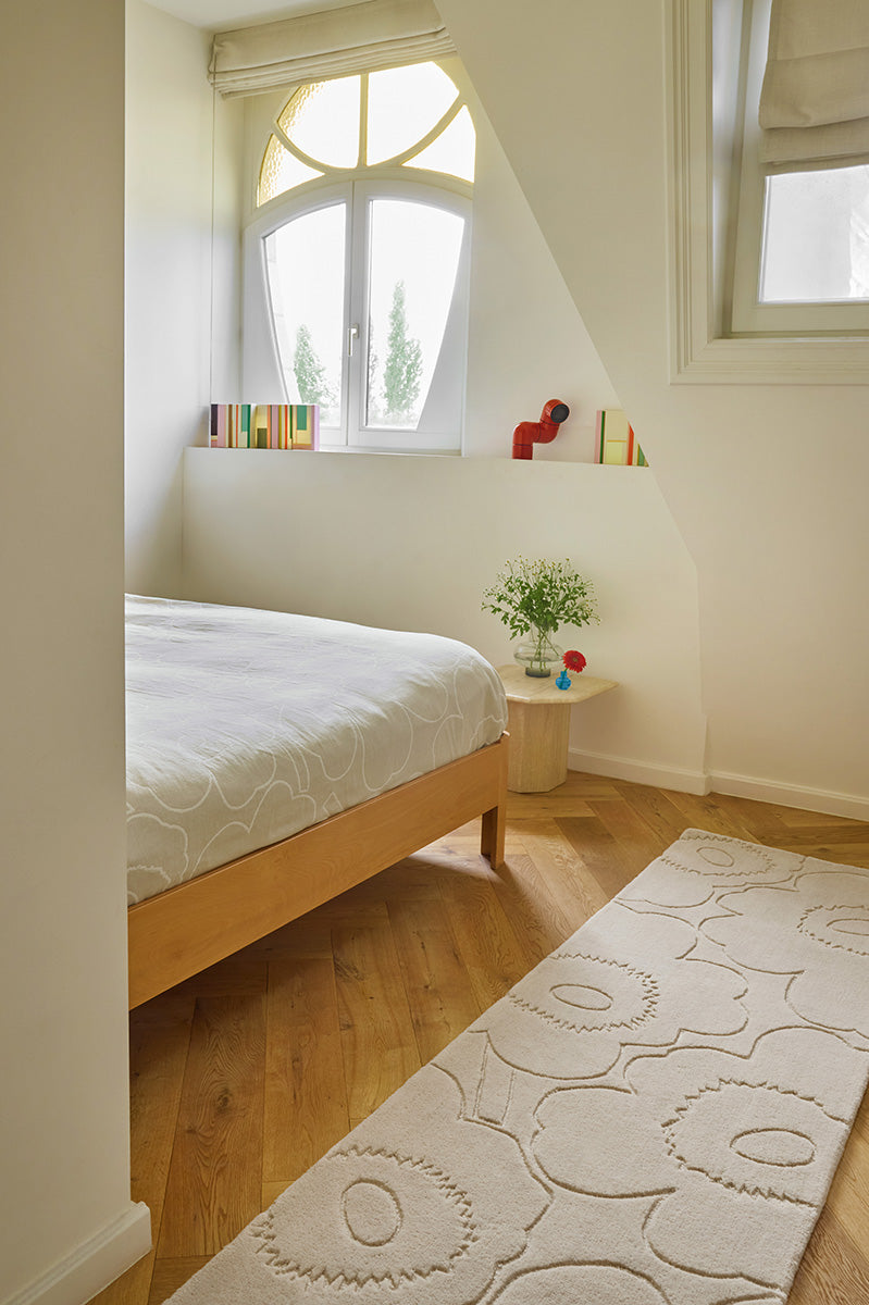 Bedroom with wooden bed, white bedding, and a creamy-white Marimekko runner rug 