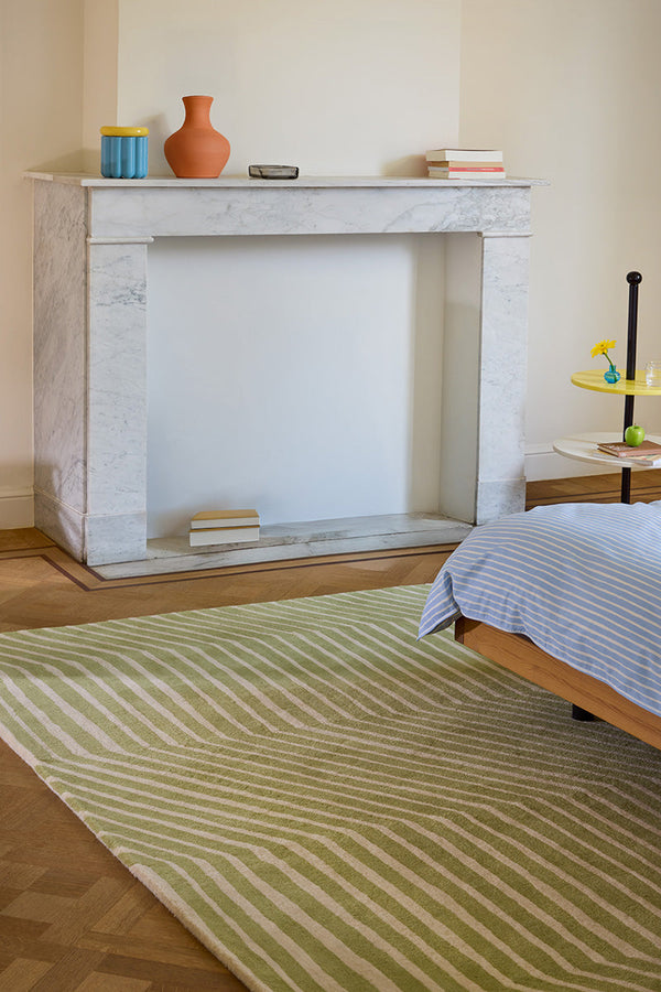 Bedroom with a Marimekko geometric green striped rug, wooden bed, and marble fireplace.