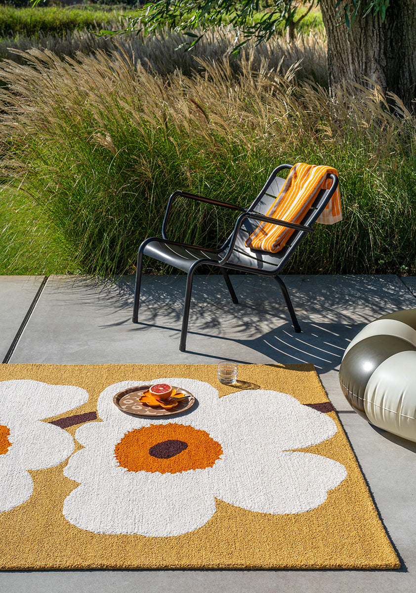 Outdoor setting with a chair on an outdoor  rug featuring the iconic Marimekko Unikko floral design in orange and white