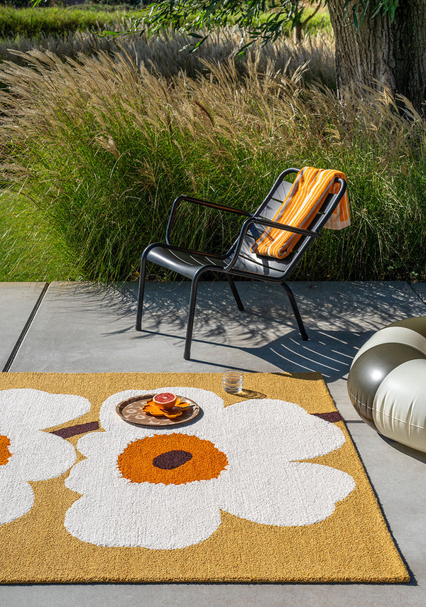 Outdoor setting with a chair on an outdoor  rug featuring the iconic Marimekko Unikko floral design in orange and white