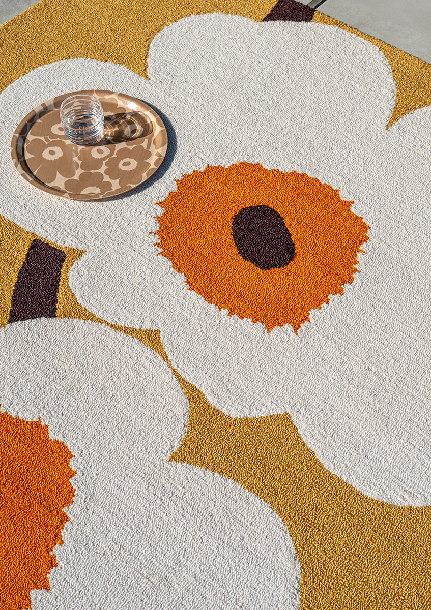 Marimekko Unikko floral-patterned outdoor rug with white flowers and orange centers on a mustard background