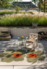 Outdoor patio with Marimekko floral outdoor rug, chair, and small table in a garden setting.