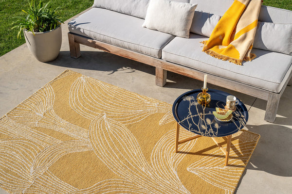 Outdoor patio with a yellow patterned Marimekko rug, grey sofa, and small table with decor items.
