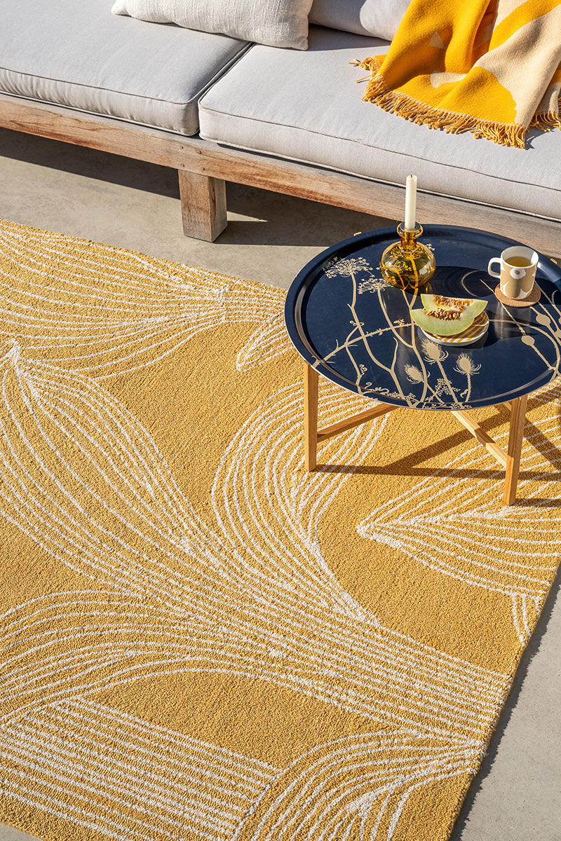 Outdoor setting with a Marimekko yellow patterned rug, wooden bench, and small table.