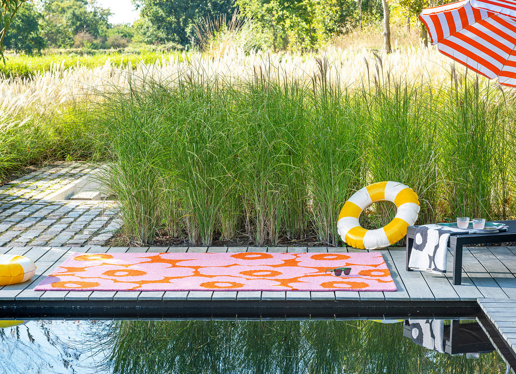 Outdoor setting with a pool featuring a Marimekko Unikko pink and orange outdoor rug