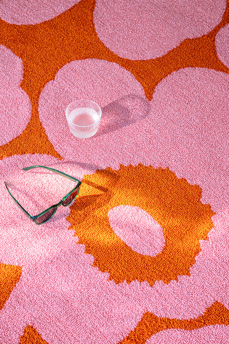 Maimekko pink and orange patterned outdoor rug with a clear glass and sunglasses on top