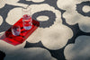 Two glasses of water on a red tray with a Marimekko Unikko  floral-patterned black and beige rug in the background