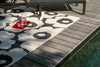 Marimekko Outdoor patterned rug on a wooden deck by a poolside with a glass of water on a red coaster.