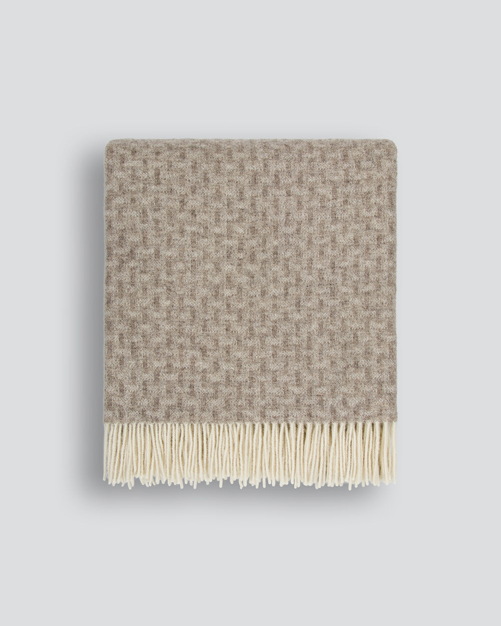 Patterned wool blanket with fringe on a light gray background