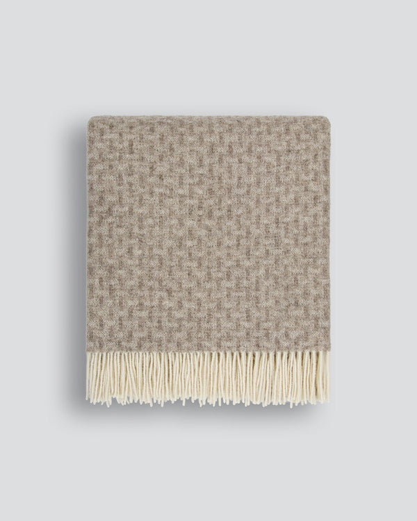 Patterned wool blanket with fringe on a light gray background