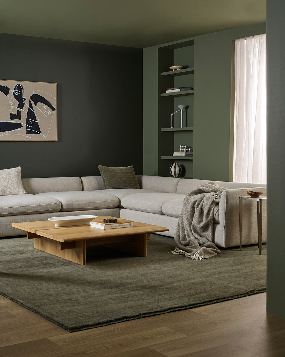 Modern living room with a gray sectional sofa, coffee table, green wool rug and patterned wool throw