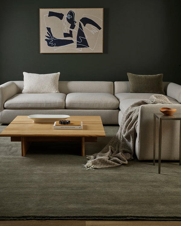 Modern living room with a sectional sofa, coffee table, green wool rug and patterned wool throw