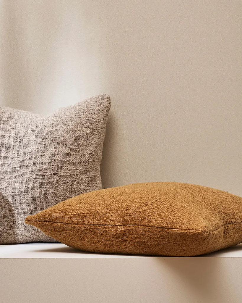 Baya designer cushion 'Cyprian' in a caramel brown tone, next to another cushion in a neutral colour