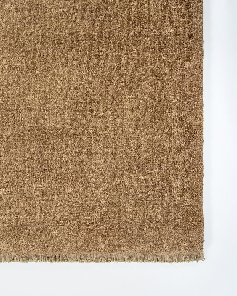 The Baya Sandringham light-mid brown 'Fenugreek' wool rug, seen close up at the corner highlighting the fringe detail and sophiticated colour