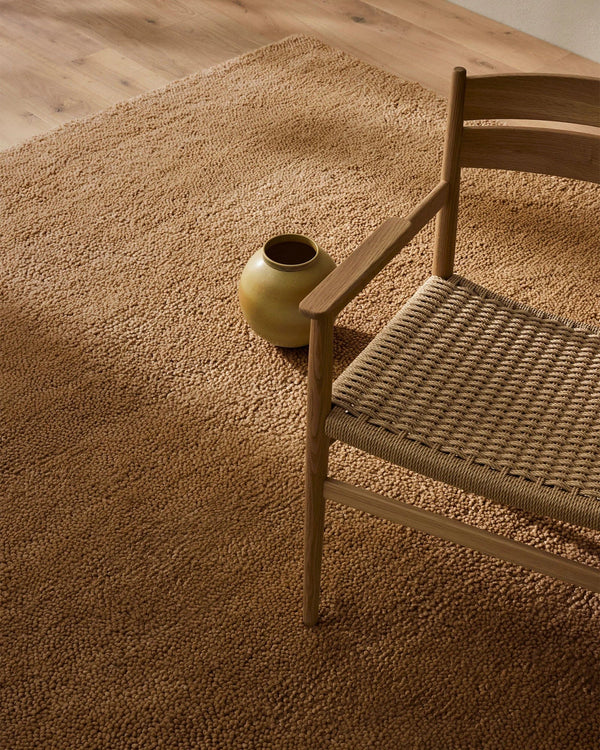 A beautiful caramel-brown wool rug, with thick and plush cut pile - the Valencia Camel, seen in a room under a  stylish chair.