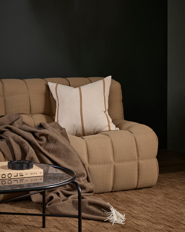 Beige sofa with a striped neutral cushion, wool throw and brown rug