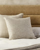 The beige Alder 'Ost' cushion by Baya NZ, seen next to a beige linen cushion on a bed in a modern bedroom.