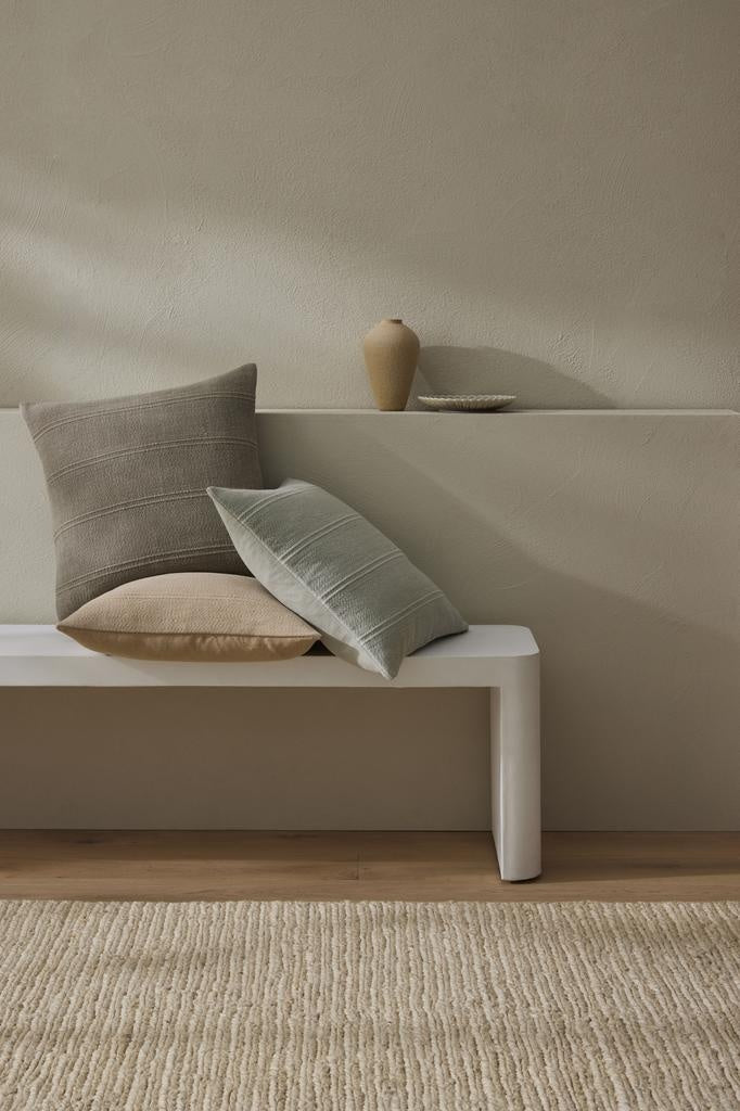 Three colours of the "Palma' cushion by Weave Home, stacked on a white bench seat.