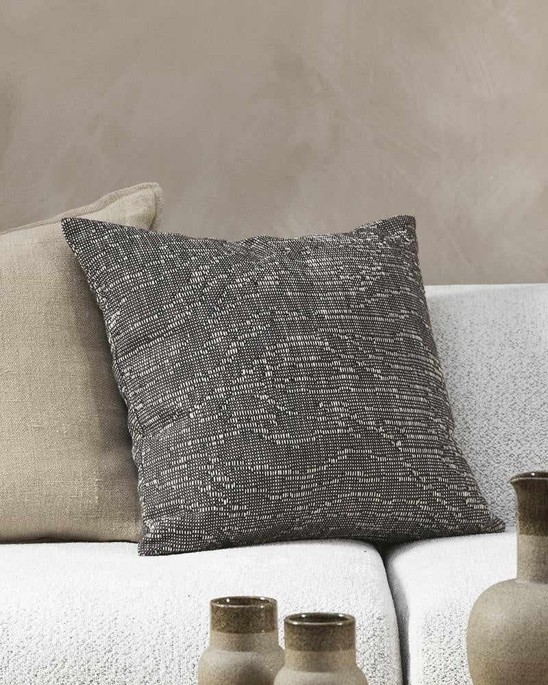 Dark chocolate coloured designer cushion on a couch in a modern home, seen close up with another cushion.