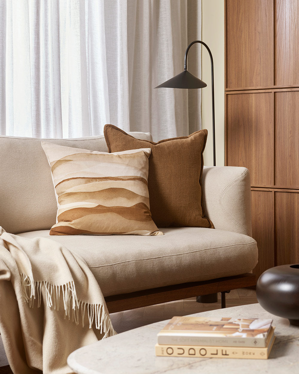 A cream coloured couch with pillows in varying shades of brown, tan, and cream, by Baya. 
